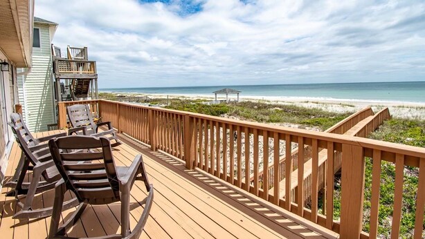 Eine Holzterrasse mit Schaukelstühlen mit Blick auf einen Strand.