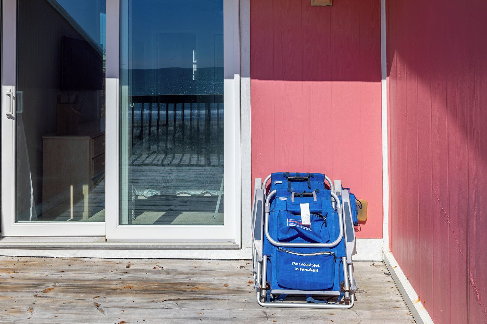 A blue suitcase on a wooden deck next to a building with a red wall and a glass door.