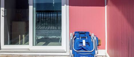 A blue suitcase on a wooden deck next to a building with a red wall and a glass door.