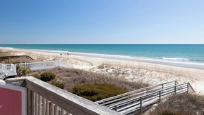 A beach view with a wooden boardwalk leading to the shore, a clear sky, and a calm sea. - 2 Seas the Day West, Oceanfront Duplex in Emerald Isle, NC! (Emerald Isle)