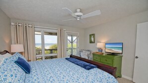 Ein Schlafzimmer mit einem großen Bett, einem Deckenventilator, einem Fernseher und Meerblick durch das Fenster.