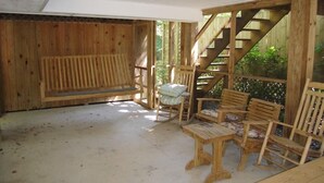 En træterrasse med en træbænk, en træstol og et lille bord. Der er en trappe i træ, der fører op til en etage.