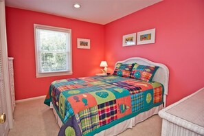 A bedroom with a colorful quilted bedspread, a white headboard, a bedside lamp, and a window with blinds. - A Herd Of Turtles, Almost Oceanfront House in Emerald Isle, NC! (Emerald Isle)