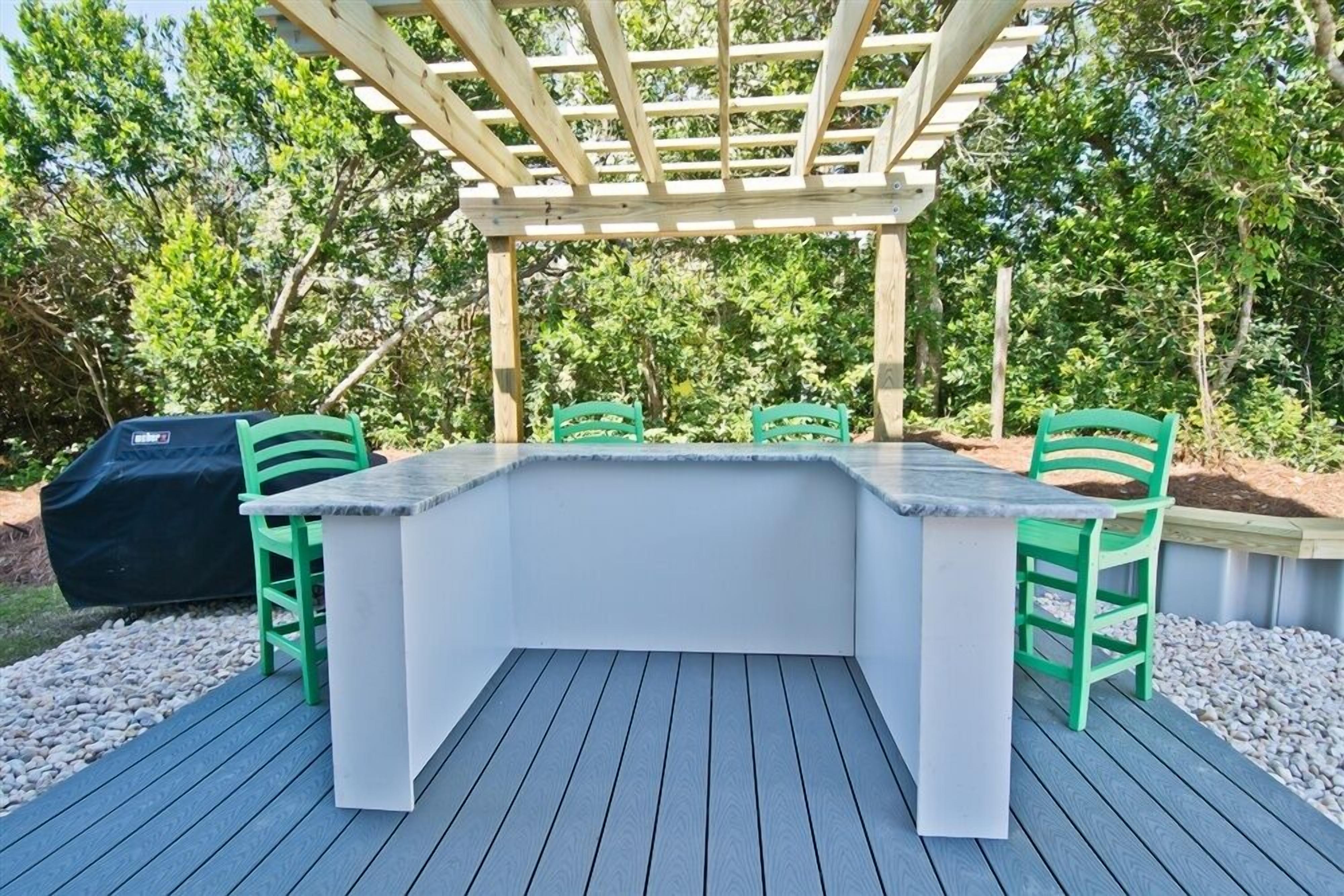 An outdoor deck with a built-in bar area, green chairs, and a grill.