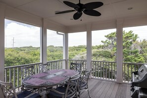 Eine überdachte Terrasse im Freien mit Tisch und Stühlen, einem Deckenventilator und Blick auf eine üppige Landschaft.