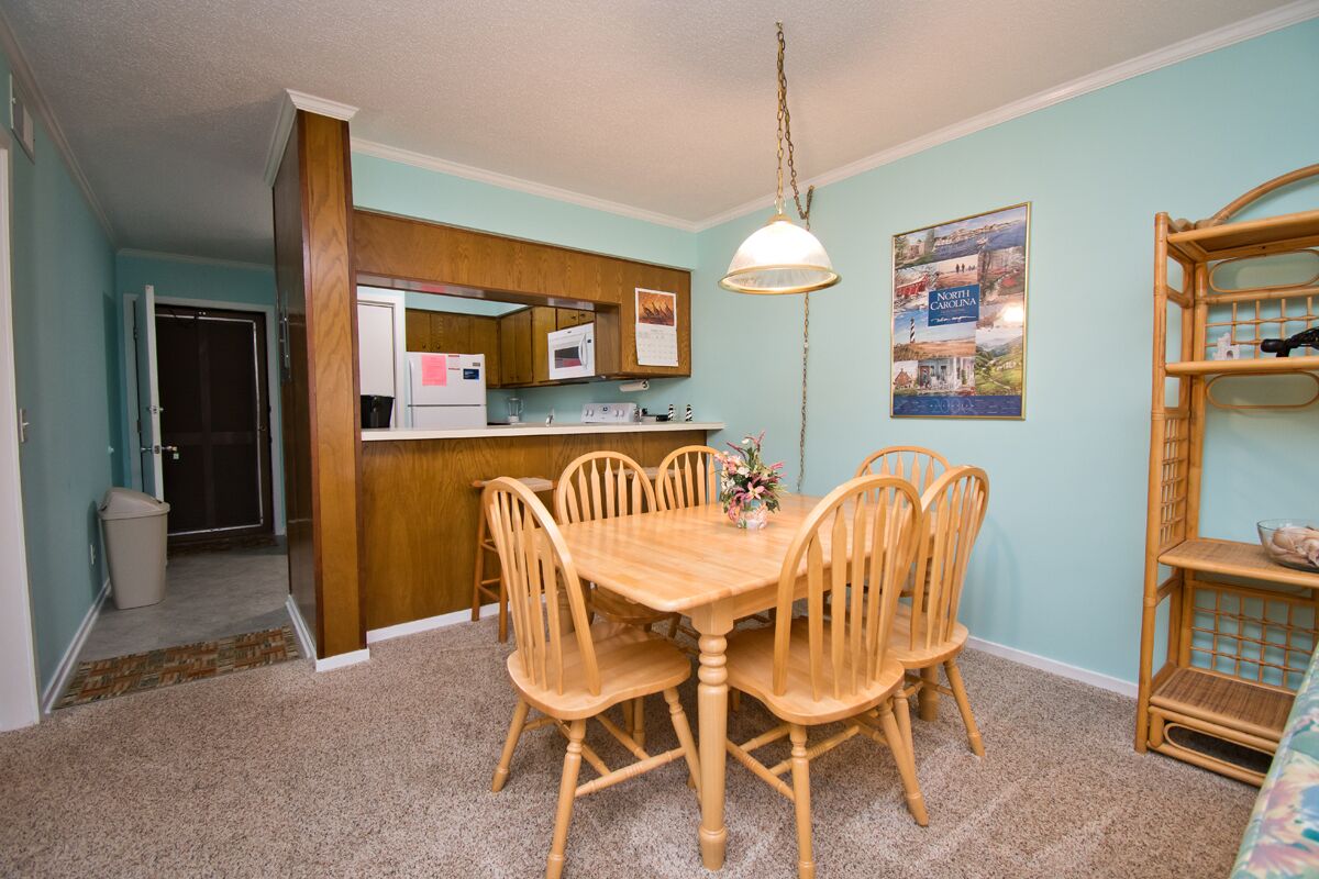 A dining area with a wooden table and chairs, a kitchen with a microwave, and a wall-mounted shelf.