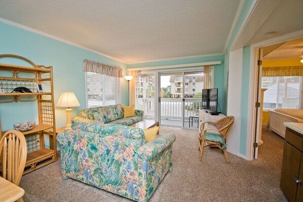 A living room with a floral sofa, a wicker chair, a small table with a lamp, and a TV.