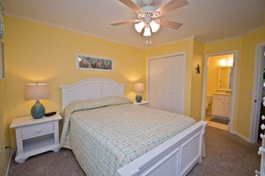 A bedroom with a bed, two bedside tables with lamps, a ceiling fan, a door, and a bathroom visible through an open door.