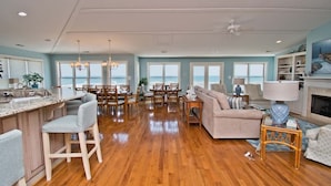 A spacious living area with a kitchen, dining area, and a large window overlooking the ocean. - A Sandy Ridge, Oceanfront House in Emerald Isle, NC! (Emerald Isle)