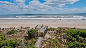 Une plage avec une promenade en bois menant à une construction, le tout entouré de dunes et de végétation.