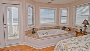 Une chambre avec une grande baignoire, un lit avec une literie à motifs floraux et une vue sur l’océan par les fenêtres.