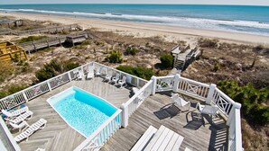 Une terrasse en bois avec une piscine, une vue sur la plage et un escalier en bois menant à un espace de plage.