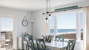 A dining area with a view of the beach, a clock on the wall, and a sign above the windows. - A Wave From it All, Oceanfront Duplex in Emerald Isle, NC! (Emerald Isle)