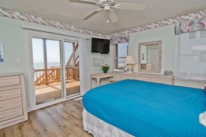 Un dormitorio con una cama grande, ventilador de techo, televisor y balcón con terraza de madera.