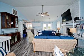 Un salon avec un canapé bleu, des meubles en osier, un ventilateur de plafond, un téléviseur et une cheminée.