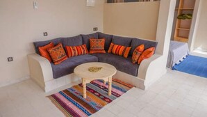 Ein Wohnzimmer mit einem grauen Ecksofa, bunten Kissen, einem kleinen runden Tisch und einem gestreiften Teppich.