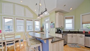Una cocina con una isla central, muebles blancos y vistas al exterior a través de amplias ventanas.