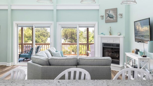 A living room with a sectional sofa, a fireplace, a television, and large windows.