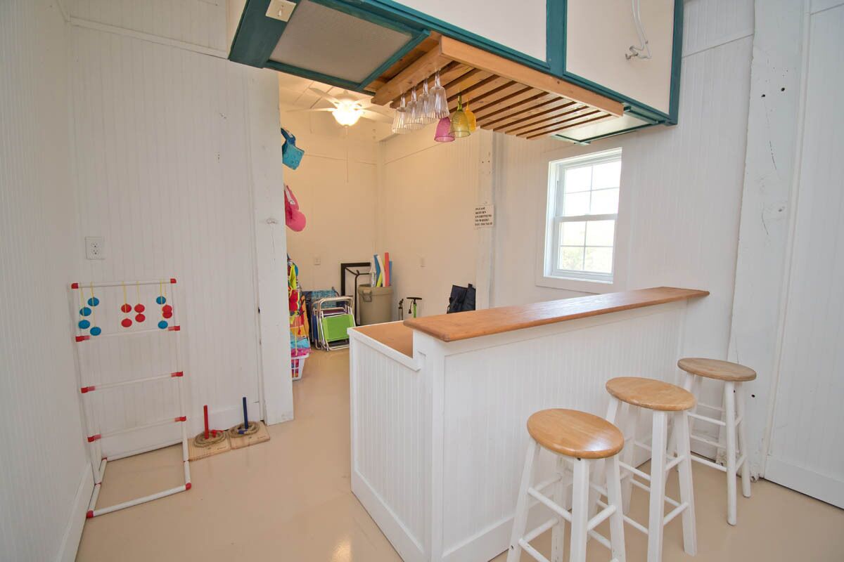 A kitchen with a wooden counter, three stools, a hanging light fixture, and a window.