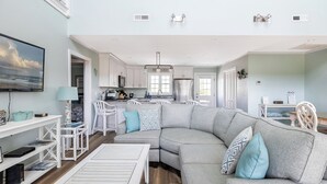 A modern living room with a sectional sofa, a TV, and a dining area with a table and chairs.