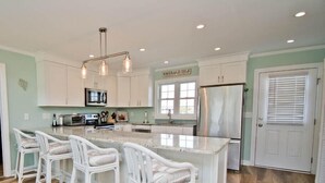 A modern kitchen with white cabinetry, a central island with bar stools, stainless steel appliances, and a sign reading "Emerald Isle".
