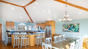 A spacious kitchen with wooden cabinets, a central island with bar stools, a dining area with a glass table, and a ceiling fan. - Angel's Dream, Oceanfront House in Emerald Isle, NC! (Emerald Isle)