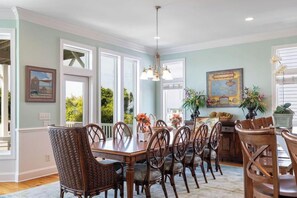 A dining room with a large wooden table and chairs, large windows, and a chandelier. - Angel's Haven, Oceanfront House in Emerald Isle, NC! (Emerald Isle)
