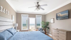 Une chambre avec un lit, un ventilateur de plafond, une commode, une télévision et une vue sur la plage.