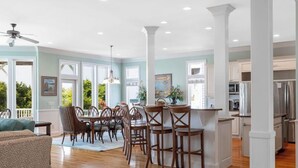 Une cuisine spacieuse avec des meubles blancs, un îlot central et un coin repas comprenant des chaises et une table en bois.