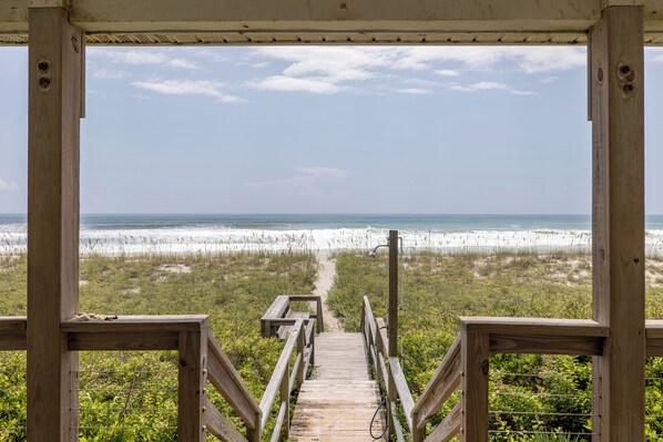 A wooden boardwalk leading to a beach with a clear view of the ocean and sand dunes.