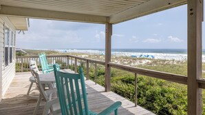 A wooden deck with a table and chairs, overlooking a beach with dunes and umbrellas. - Anniversary Waltz East, Oceanfront Duplex in Emerald Isle, NC! (Emerald Isle)