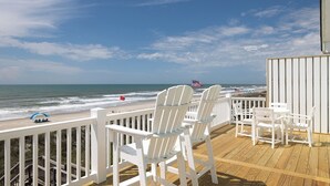 Terraza de madera con sillas y una mesa blancas, con vistas a la playa.