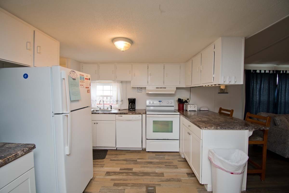 A compact kitchen with white cabinets, a refrigerator, a stove, and a sink.