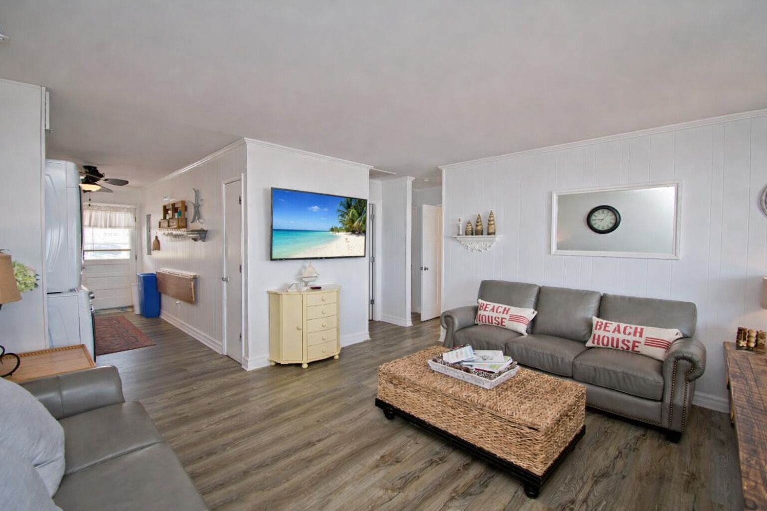 Uma sala de estar com sofá, mesa de centro, televisão e um quadro de uma cena de praia.