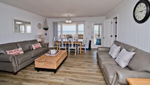 A living room with two sofas, a dining table, and a view of the beach. - At Anchor East, Oceanfront Duplex in Emerald Isle, NC! (Emerald Isle)