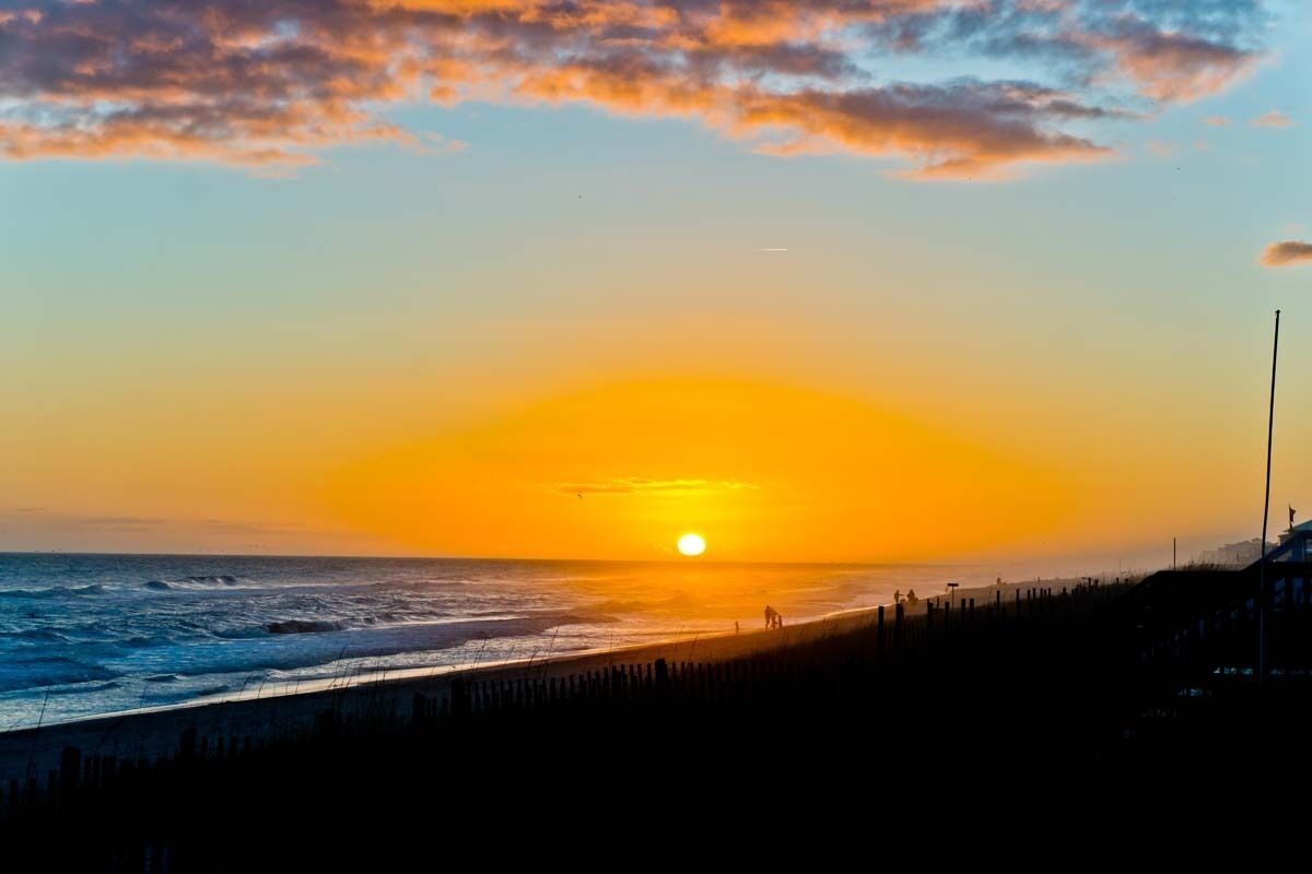 A beach with a sunset, a fence, and a building in the background.