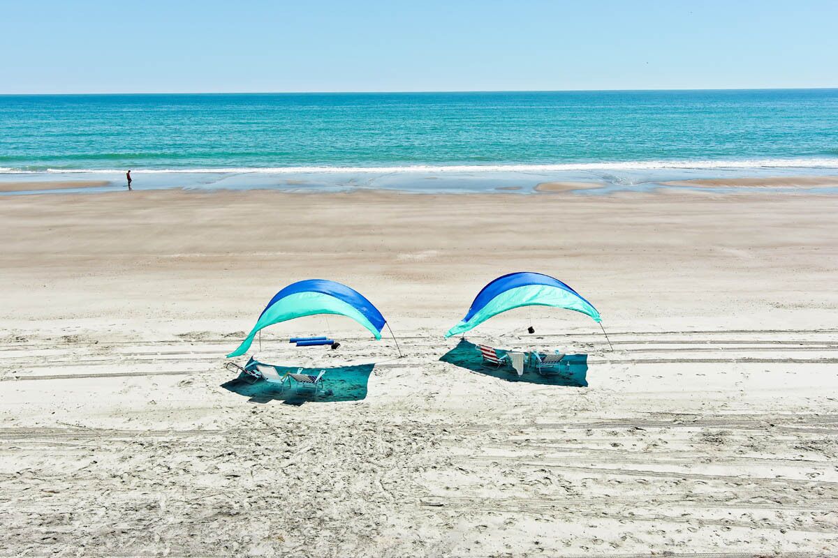 Une plage avec deux parasols bleus et une personne au loin.