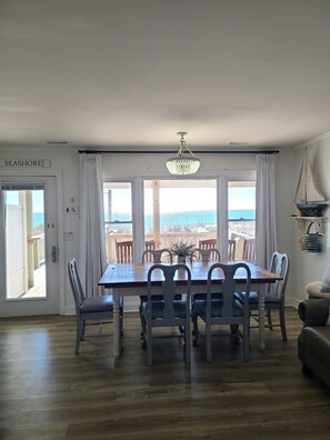 Un comedor con mesa y sillas de madera, una araña y vista al mar.