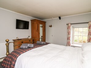 Une chambre à coucher avec un grand lit, une commode en bois, un téléviseur à écran plat et une fenêtre avec des rideaux.