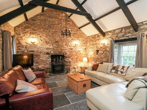 Una sala de estar acogedora con paredes de piedra, chimenea, sofás de cuero y televisión.