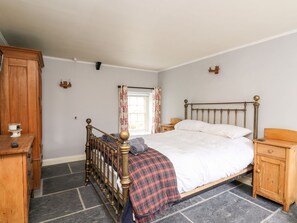 Une chambre à coucher avec un lit en bois, une table de chevet, une armoire en bois et une fenêtre avec des rideaux.