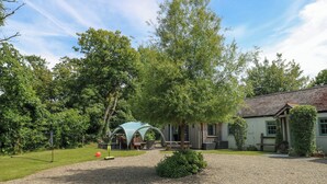 A gravel driveway leading to a house with a covered outdoor seating area and a tennis court.