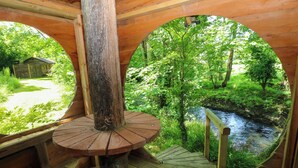 A wooden structure with a circular window overlooking a river and greenery.