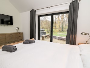 Ein Schlafzimmer mit einem großen Bett, einer Holzkommode, einem Flachbildfernseher und Blick auf einen Garten durch eine Schiebetür.