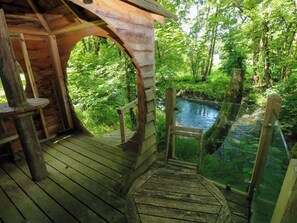 Un pontile in legno con ringhiera in vetro che si affaccia su un fiume, immerso nel verde.
