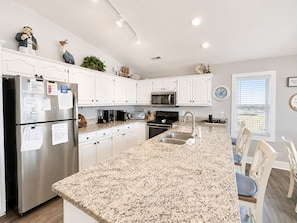 A modern kitchen with white cabinets, granite countertops, a stainless steel refrigerator, a microwave, and a sink. - Atlantic Sea Oats, Oceanfront Duplex in Emerald Isle, NC! (Emerald Isle)