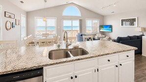 A spacious kitchen with a large island, a dining area with a view of the ocean, and a living area with a TV and seating. - Atlantic Sea Oats, Oceanfront Duplex in Emerald Isle, NC! (Emerald Isle)