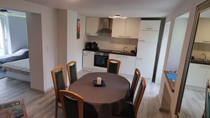 A modern kitchen with white cabinets, a dining table with chairs, and a large window providing natural light.