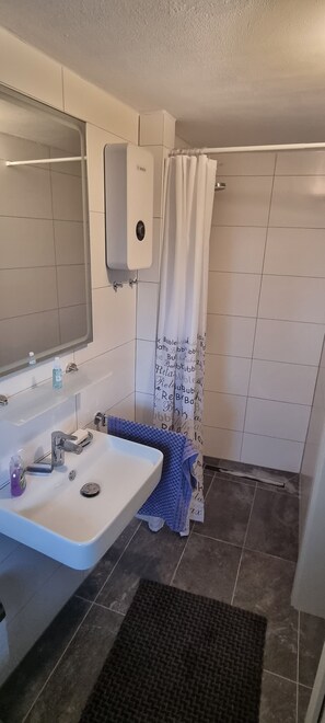 Een badkamer met een wastafel, spiegel, handdoekhouder en douchegordijn.