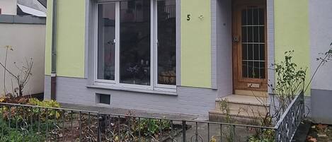 A two-story house with a light green facade, a small front porch, and a visible door.
